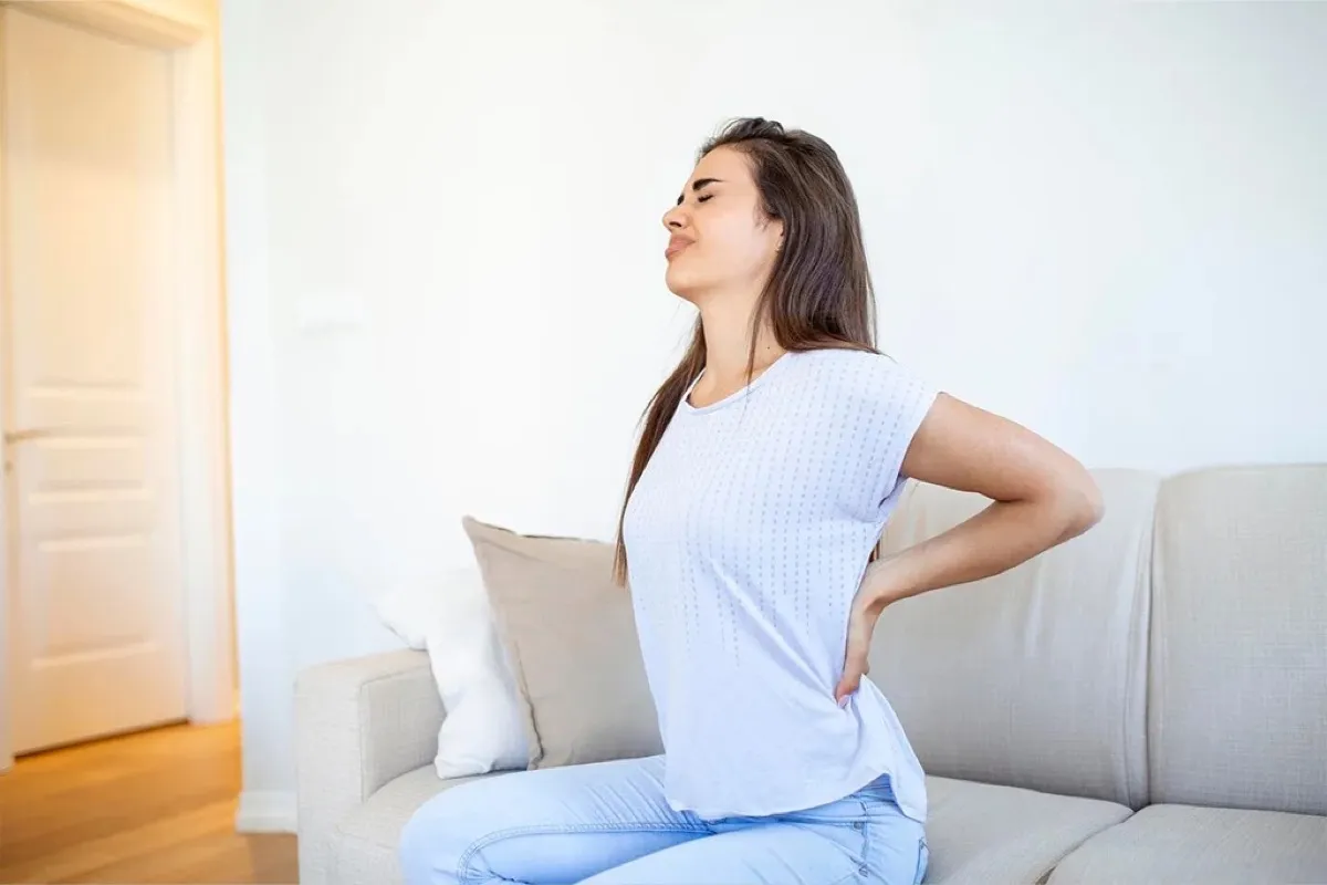 Woman sitting on a couch holding her lower back in pain during an acute low back pain episode