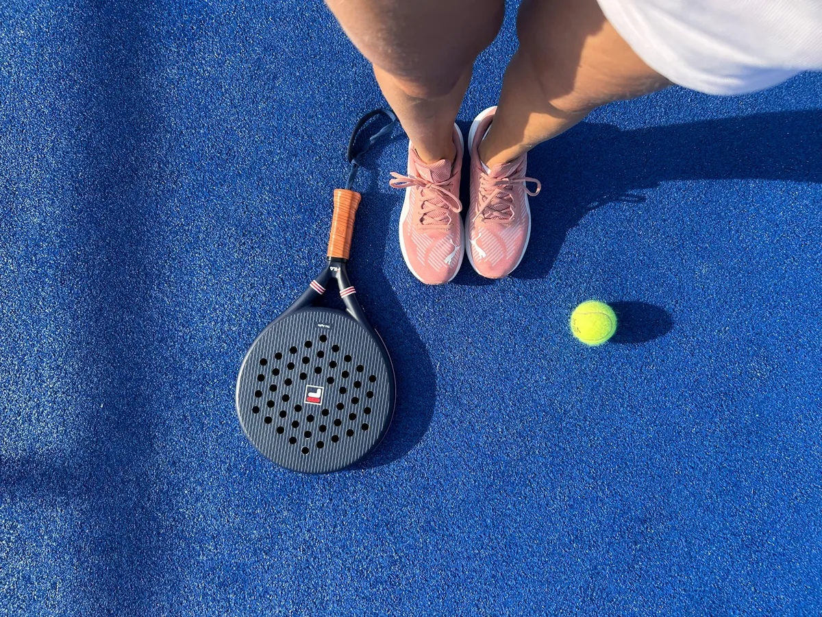 Padel racket, ball and shoes on a blue padel court