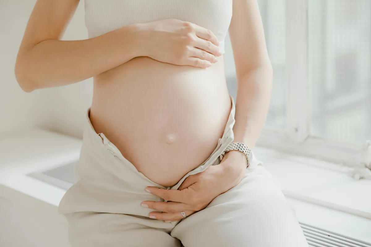 Pregnant woman cradling her belly with one hand resting at the front of her pelvis