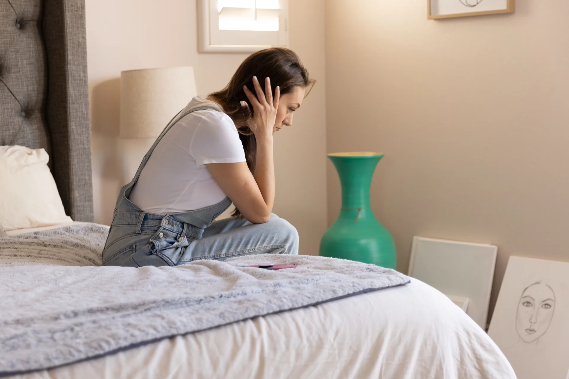 Woman sitting on the edge of her bed holding her head as dizziness sets in