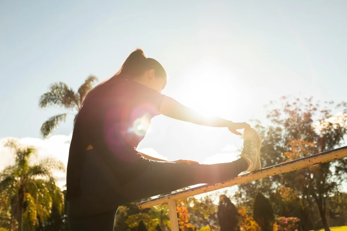 Person stretching their leg on a railing outdoors in warm sunlight